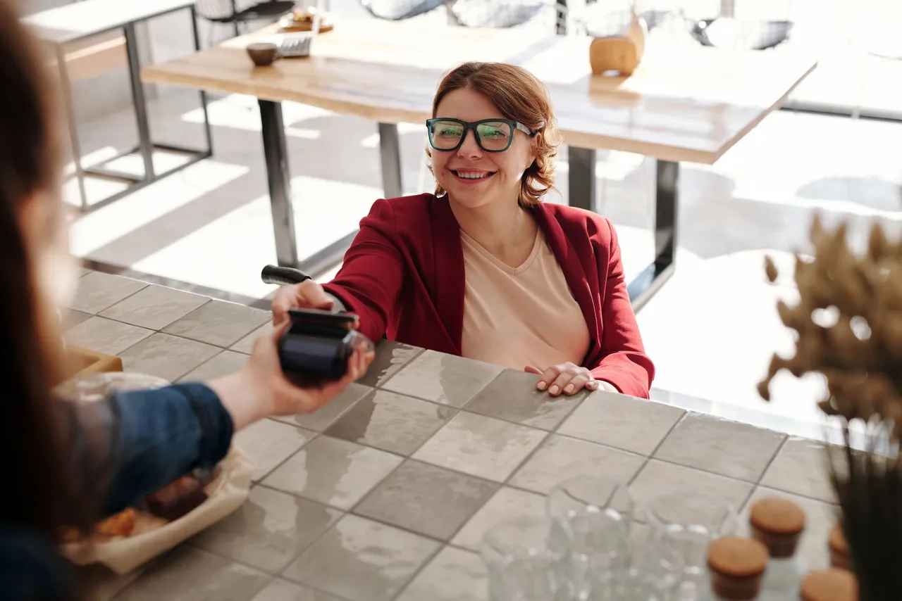 Une cliente souriante paie sans contact sur le terminal que lui tend le personnel