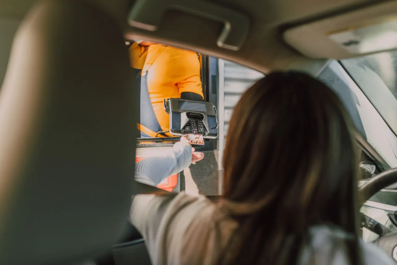 Depuis sa voiture, une conductrice tend sa carte vers le terminal de paiement tenu par un employé de la station